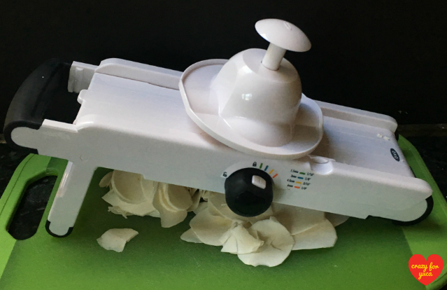 Oxo Good Grips V-Blade Mandoline Slicer over cutting board with yuca (cassava) slices.