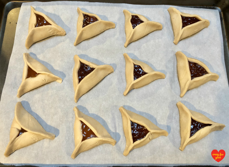 Unbaked Hamantashen on parchment lined baking sheet ready to be baked. 
