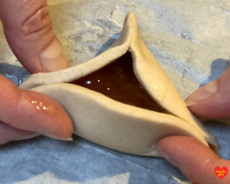 To make the second and third corners of the Hamantaschen, pick up remaining side of dough and pinch  each of the 2 edges together using both hands. 