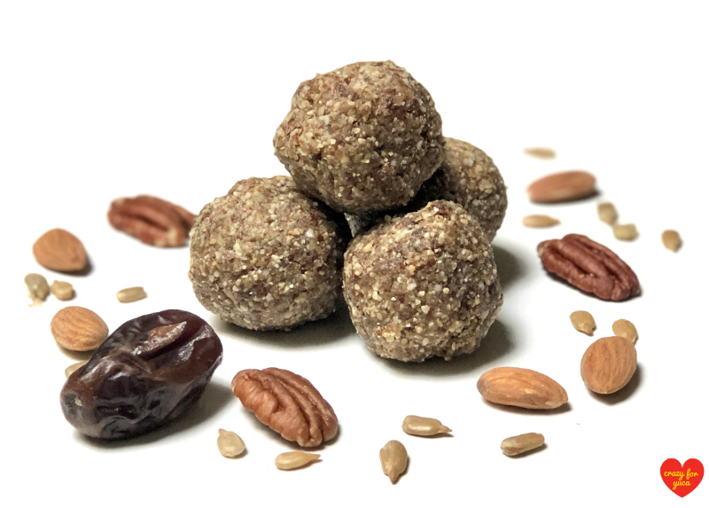 CrazyForYuca.com - 4 Paleo No-Bake Date Nut Balls stacked with scattered nuts and dates on white background.