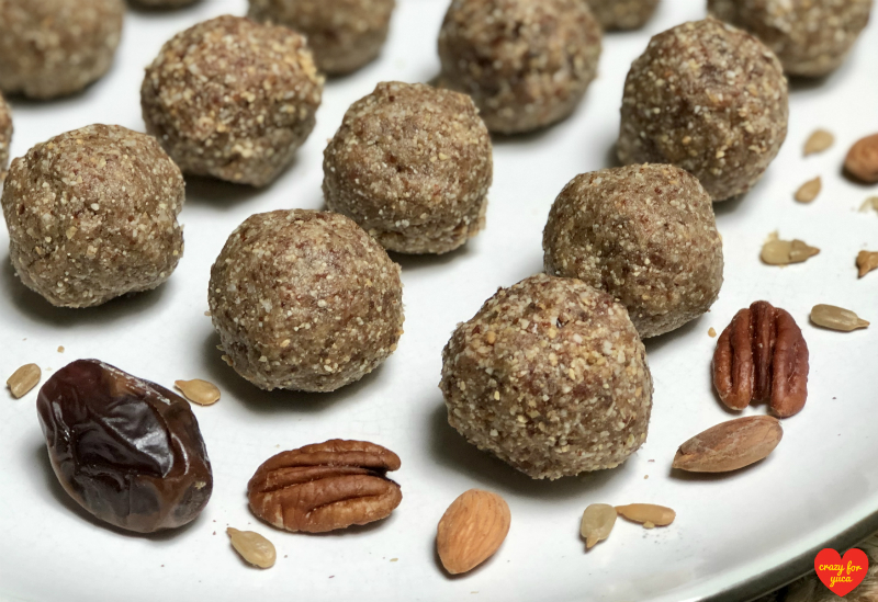 CrazyForYuca.com - Paleo No-Bake Date Nut Balls lined up on white plate with scattered nuts and dates. 