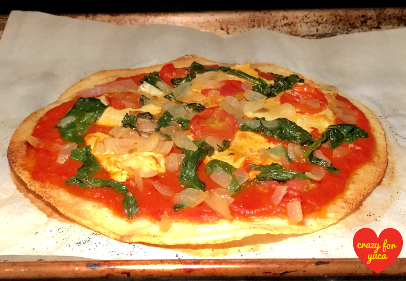 Paleo Yuca Pizza with Vegan Cheese coming out of the oven on parchment lined baking sheet.