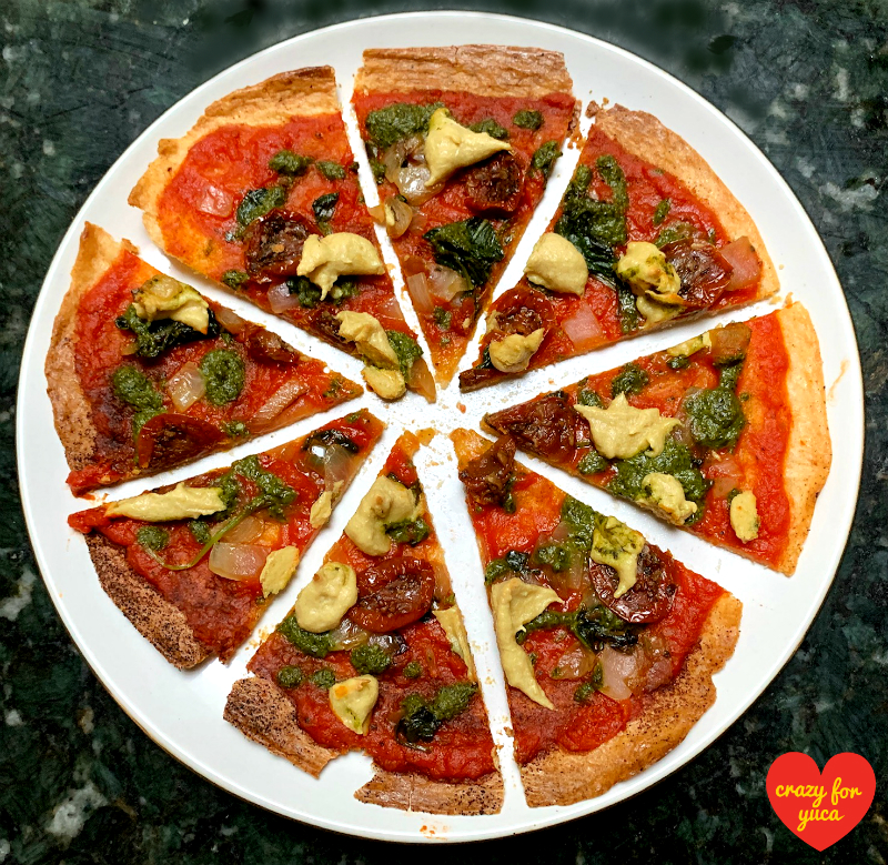 Whole Yuca Pizza with Vegan Cheese sliced on white plate.